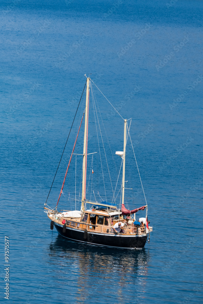 Fototapeta premium Boat whith flagpole on the water surface against the backdrop of the hill