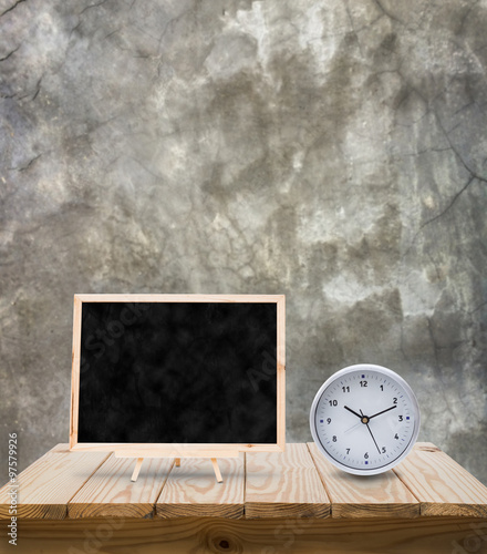 Blackboard and clock on wood table with grunge cement wall backg