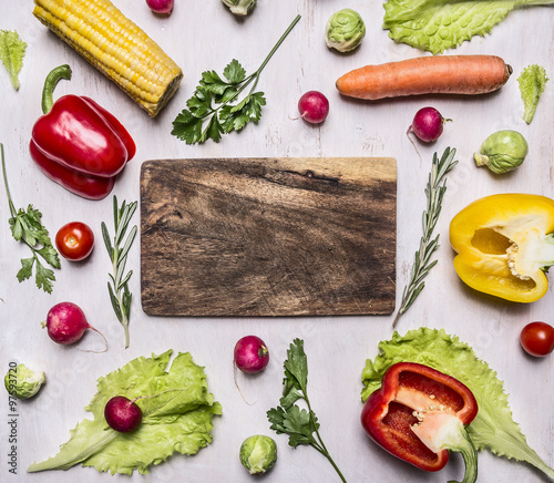 Fresh vegetables, tomatoes, peppers, basil, parsley, corn, salad laid out around a cutting board on wooden rustic background top view close up border ,with text area