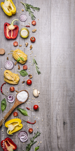 Ingredients for cooking raw pasta with tomatoes, pepper, a wooden spoon, salt, oil, pine nuts and herbs on wooden rustic background top view border ,place for text