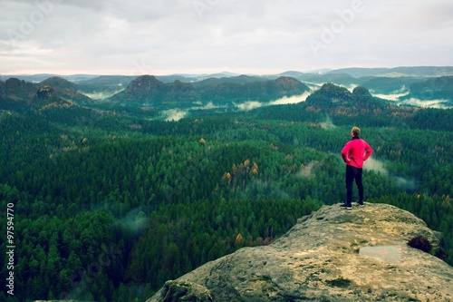 Runner in pink jacket and light black trousers. Short ginger hair man in his target. Tired sportsman take a rest on thepath in rocks.