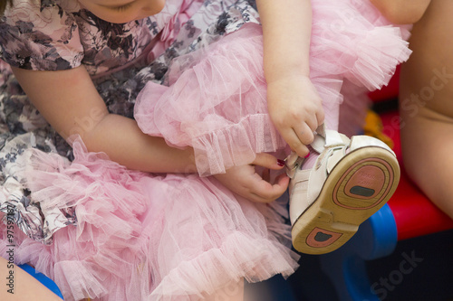 Маленькая девочка в пышном платье застегивает туфельку