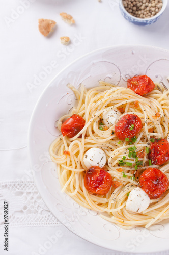 Italian spaghetti pasta with baked cherry tomatoes, mozzarella and spring onions in a white bowl on a white table. Top view.