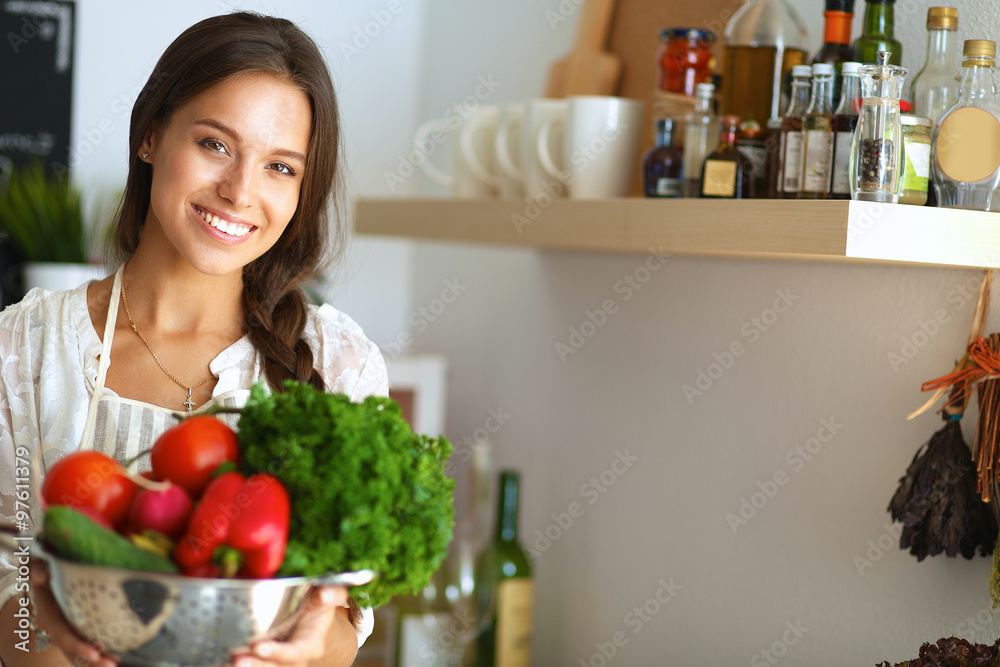 Smiling young woman holding vegetables standing in kitchen