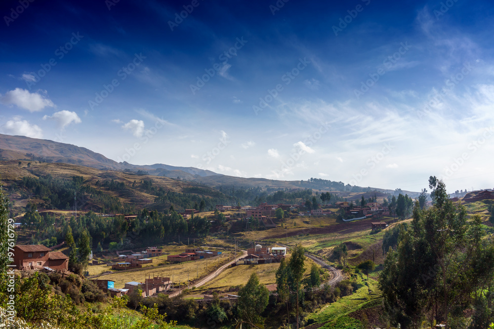 Village on hill with mountain in background against cloudy sky, Cusco, Peru