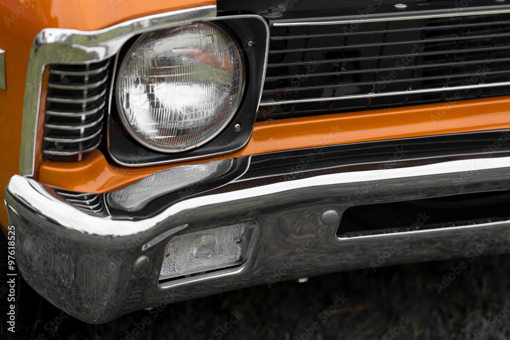 Close-up of left headlight of an orange shiny classic vintage car