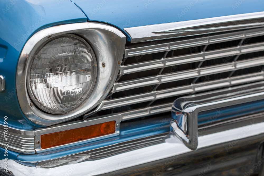 Close-up of left headlight of a blue shiny classic vintage car