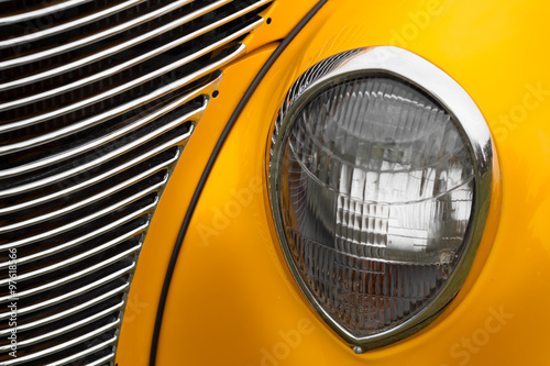 Close-up of right headlight of a yellow shiny classic vintage car