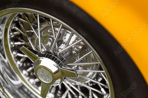 Close-up of spoke wheel of a yellow shiny classic vintage car