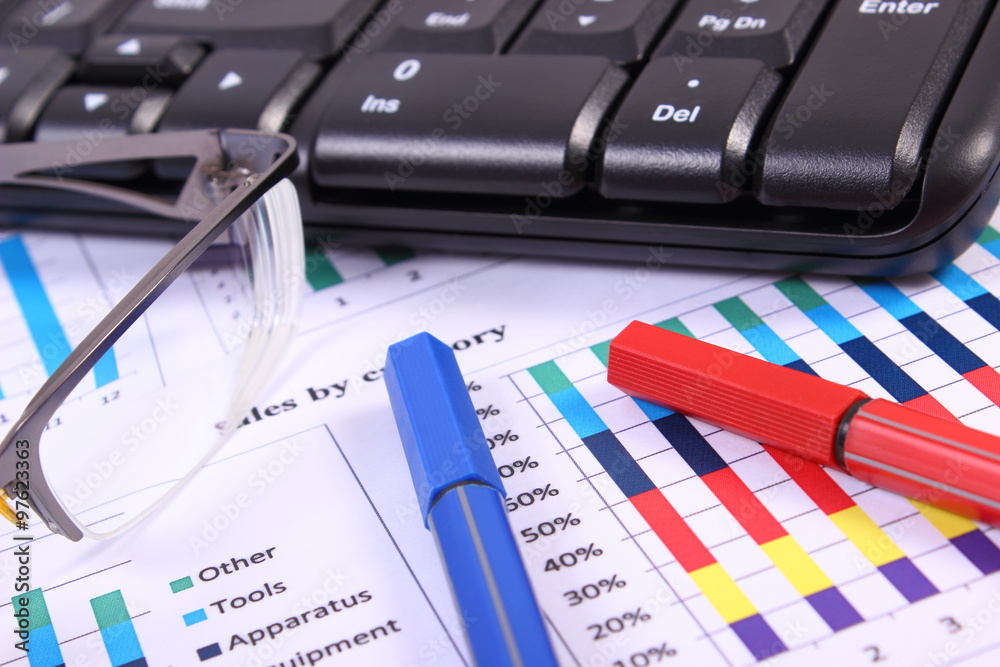 Pen, glasses and computer keyboard on financial graph, business concept