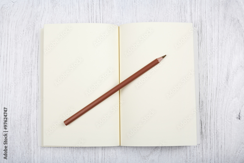 Open brown notebook and a pencil on white wooden table, top view