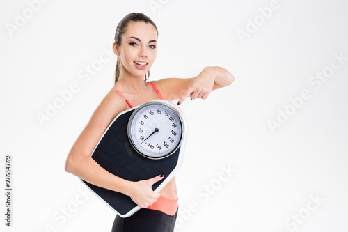 Pretty fitness girl holding weighing scale and pointing on it