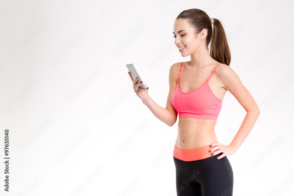 Pretty smiling young fitness woman using cellphone isolated