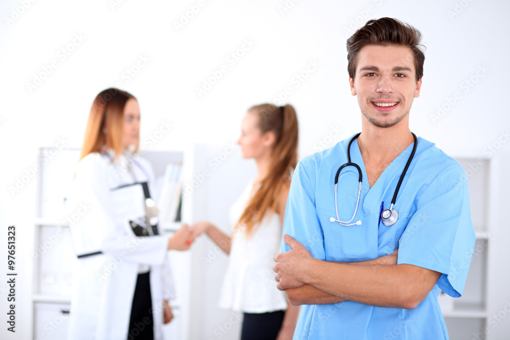 Attractive male doctor in front of medical group, crossed arms Attractive male doctor in front of medical group, crossed arms