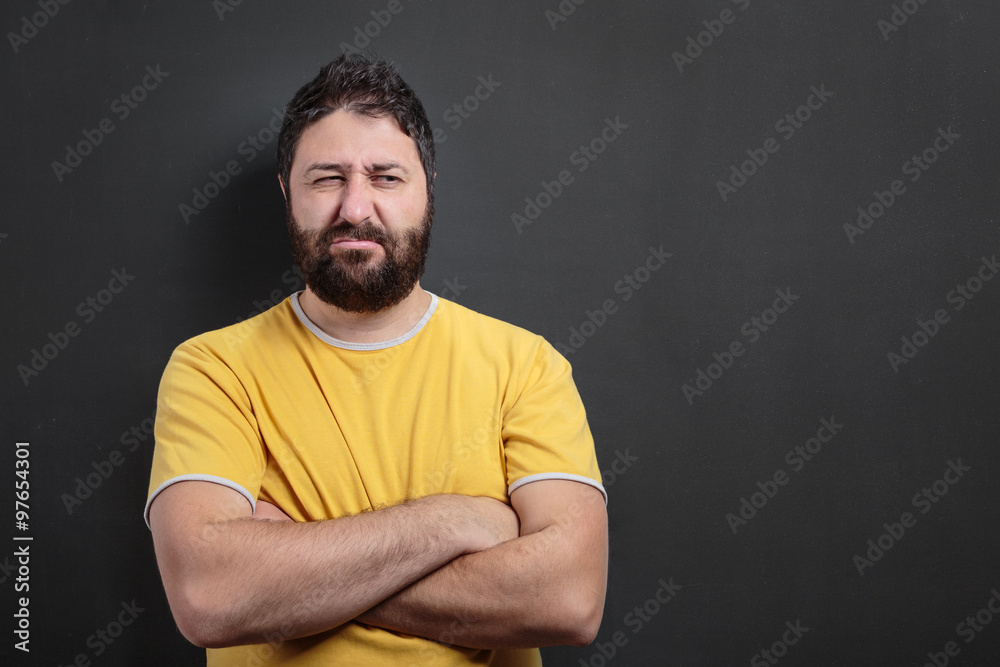 Disgruntled young man standing in front of dark chalkboard Disgruntled young man standing in front of dark chalkboard