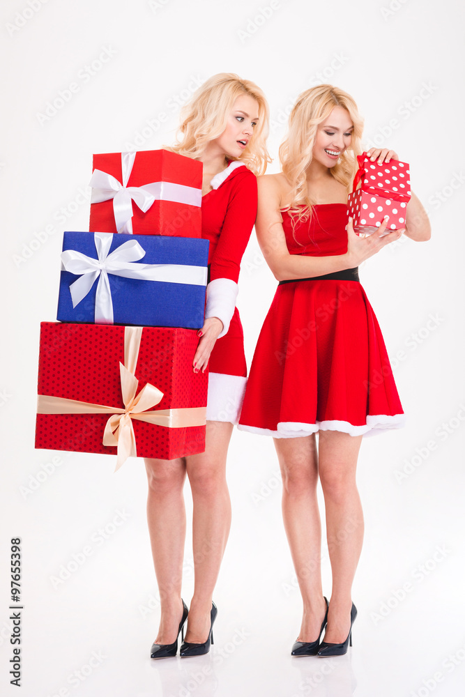 Two sisters twins in santa costumes holding and opening presents Two sisters twins in santa costumes holding and opening presents