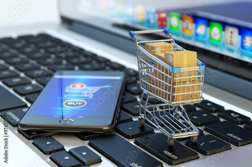 Online shopping, internet purchases and e-commerce concept, modern mobile phone with buy button on the screen and shopping cart full of package boxes on computer laptop keyboard photo