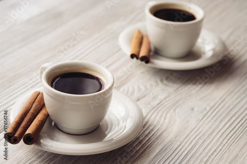 Cups of coffee with cinnamon sticks on a white wooden background