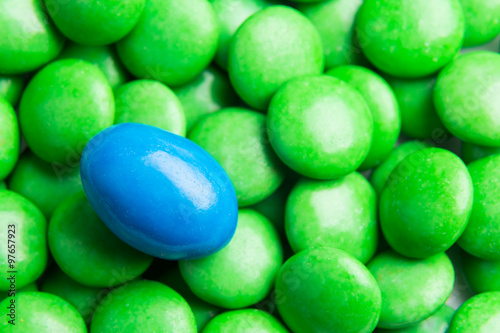Concept of selective focus on blue chocolate candy against heaps of green candies at background