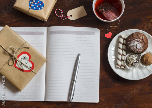 Open a clean blank Notepad, Valentines Day homemade gifts, a Cup of tea and sweets on wooden brown table. Top view, free space for text