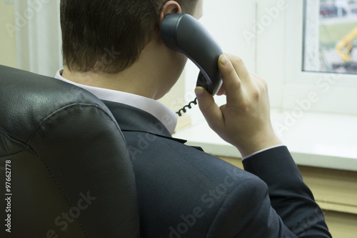 A man in a suit sitting in a chair and talking on the phone