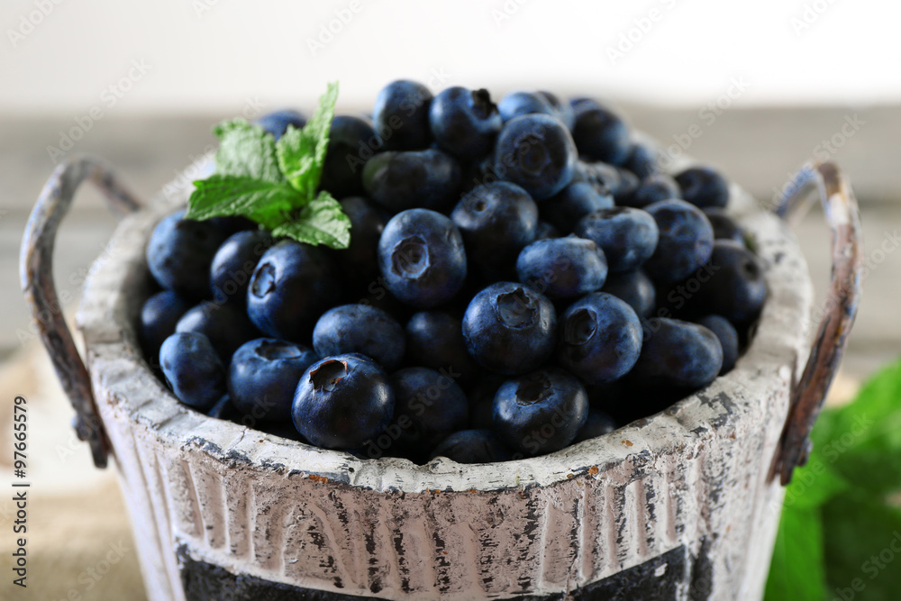 Tasty ripe blueberries with green leaves in bucket on table close up