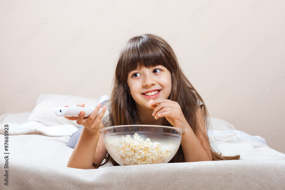 Little girl is watching tv and eating popcorn in her bed. Little girl is watching tv and eating popcorn in her bed.