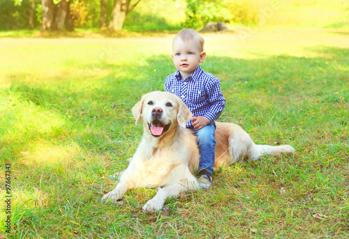Little boy child sitting on Golden Retriever dog on grass
