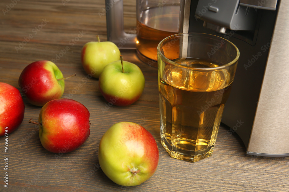 Stainless juice extractor with apples and glass of juice on wooden background, close up Stainless juice extractor with apples and glass of juice on wooden background, close up