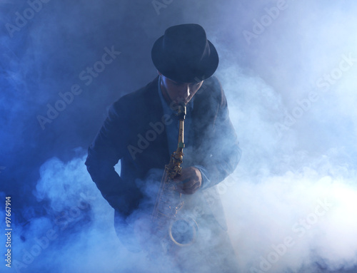 Photography Elegant saxophonist plays jazz on dark background in a smoke