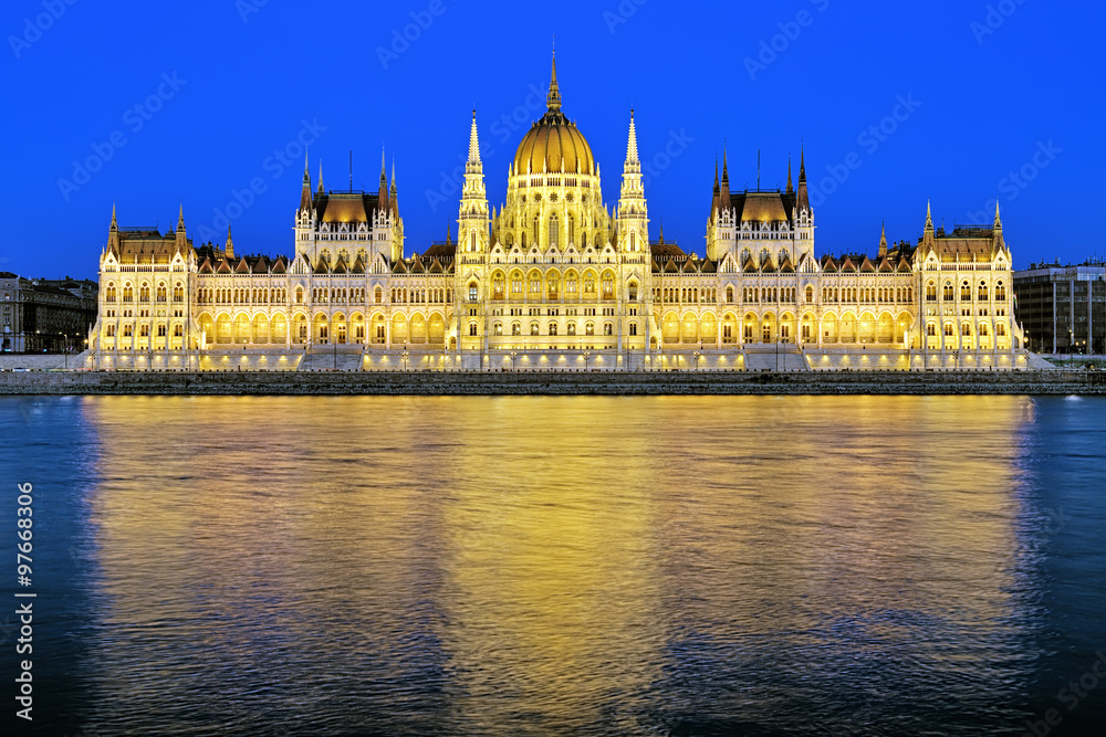 Fototapeta premium Evening view of the Hungarian Parliament Building in bright yellow illumination. View from the bank of Danube in Budapest, Hungary.