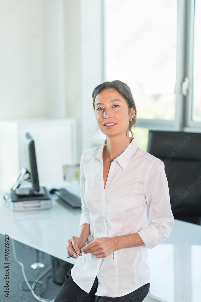 business woman leaning against her glass desk, luminous office
