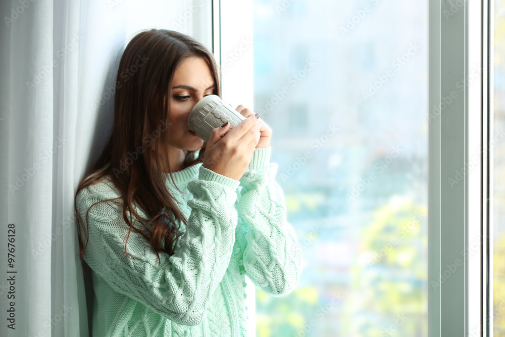 Woman drinking coffee near window in the room Woman drinking coffee near window in the room
