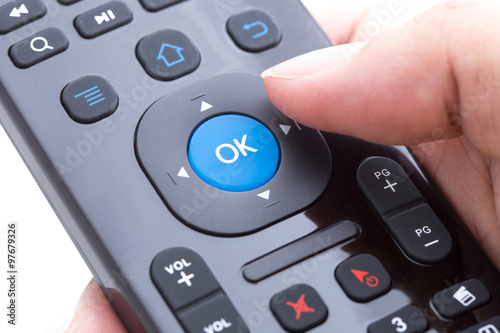 Finger will push ok button on remote control over white backgrou
