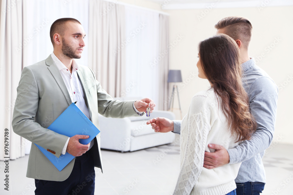 Estate agent giving keys to  couple, on light background