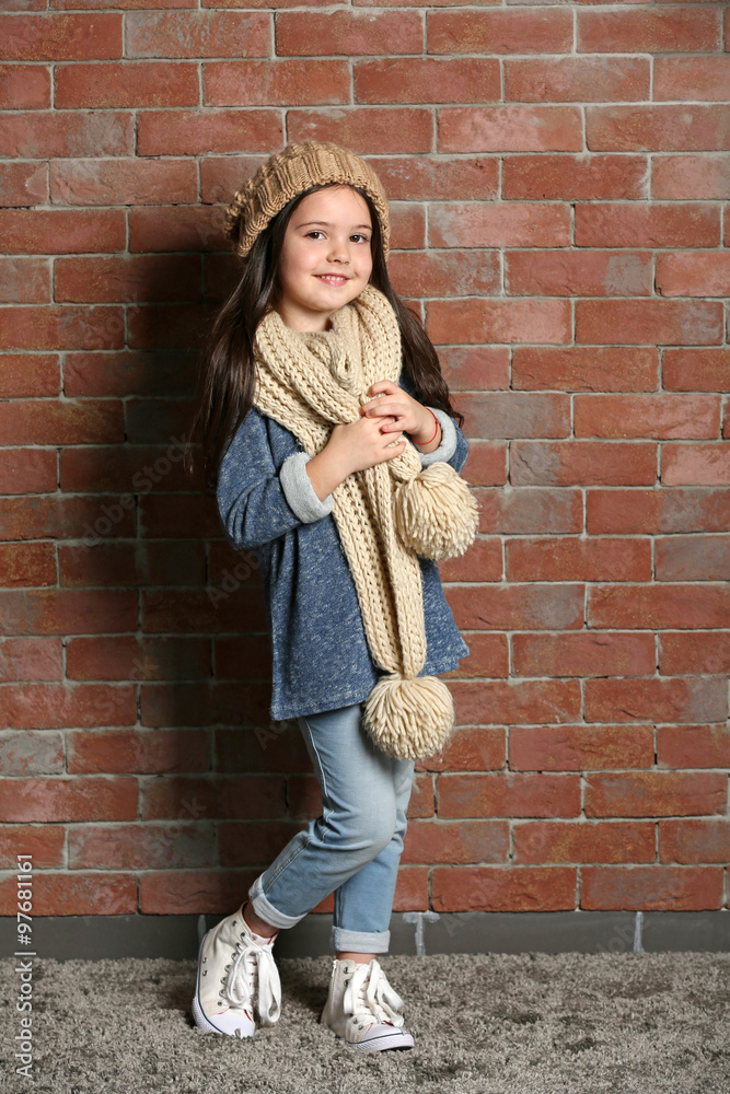 Portrait of little fashion kid girl in knitted cap and scarf on bricks wall background Portrait of little fashion kid girl in knitted cap and scarf on bricks wall background