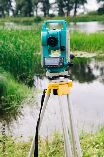 blue surveying equipment total station on a background of lake and forest