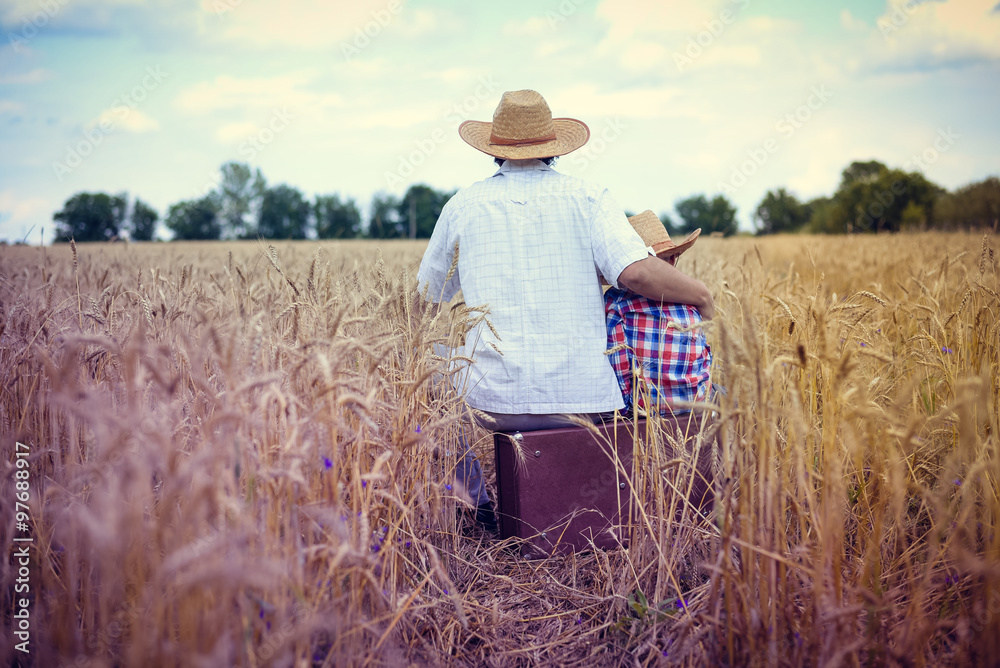 Backview of happy family sitting on old suitcase in farm field