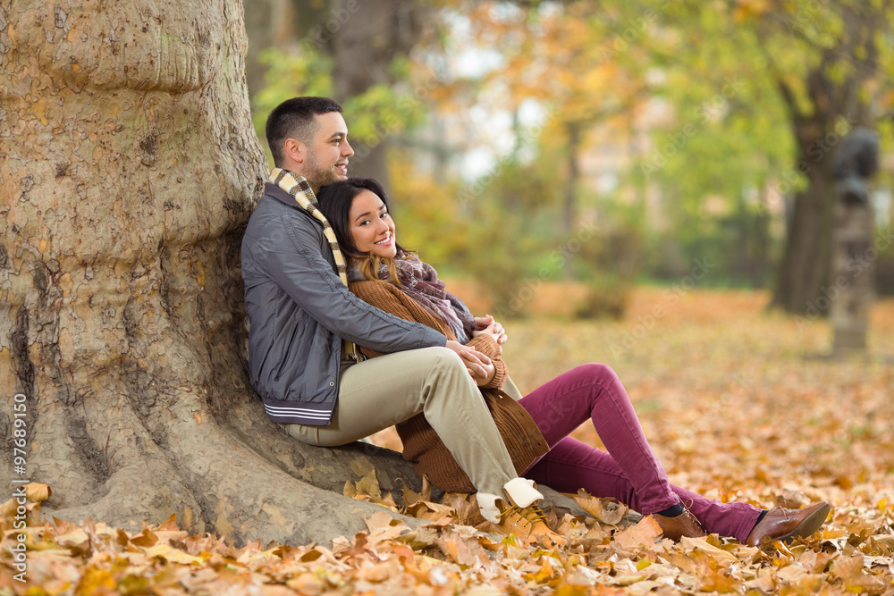 Fototapeta premium Happy young couple sitting in a park in autumn