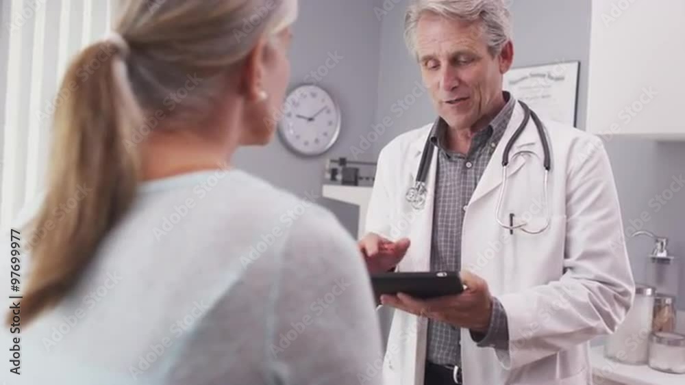 A mature doctor reviewing patient's file on a tablet A mature doctor reviewing patient's file on a tablet