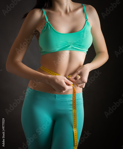 Fit and healthy young woman measuring her waist with a tape measure.
