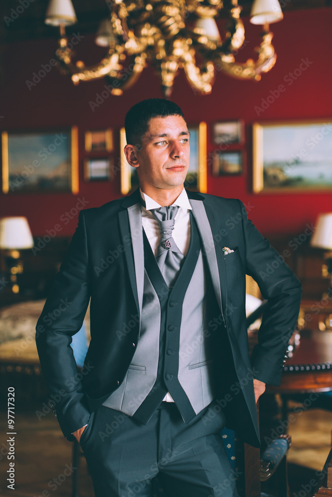 Fototapeta premium Happy groom in luxury chairs in chic interiors of wedding palace