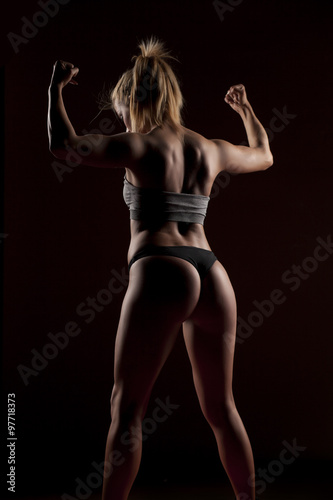 pretty woman showing her muscular body on a dark background