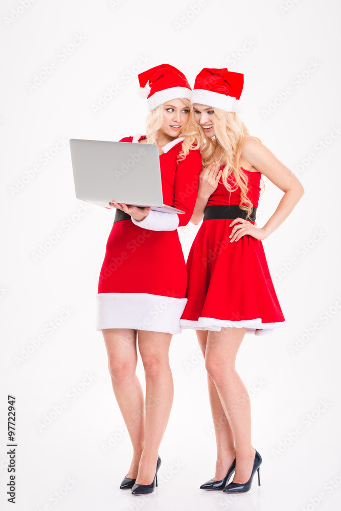 Sisters twins in santa claus dresses and hats with laptop Sisters twins in santa claus dresses and hats with laptop