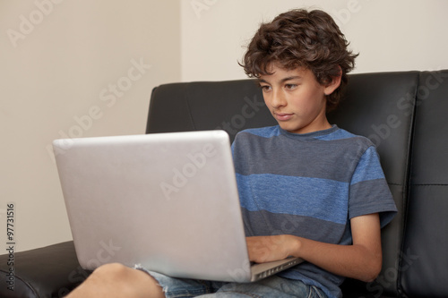 Latino boy sitting on sofa with laptop computer