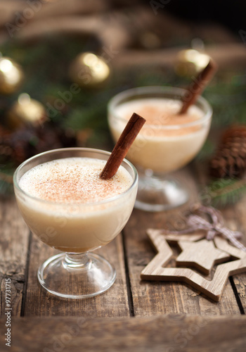 Eggnog christmas homemade winter egg, milk, rum, vanilla alcohol liqueur preparation recipe in two cups with cinnamon sticks on wooden vintage table. shallow depth of field