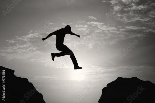 Man jumping over precipice on sunset background