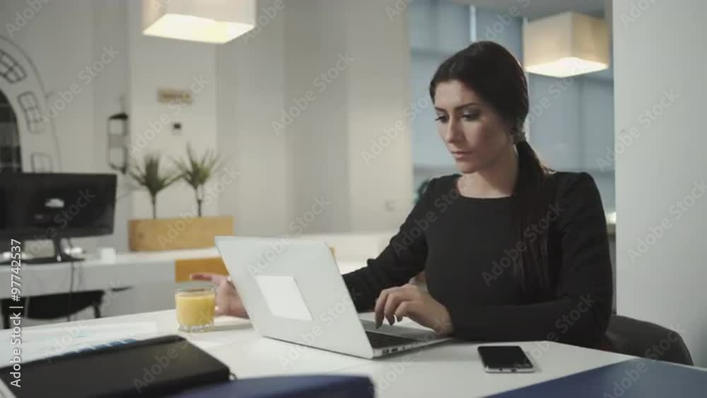 A woman working at the computer and drinking orange juice