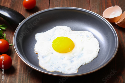 Pan of fried egg, with cherry-tomatoes and parsley on a wooden table surface