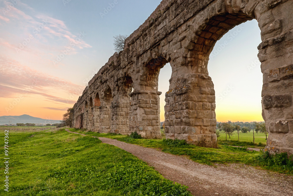 Ancient Roman aqueduct. A path runs along the property in a green park in the outskirts of Rome.